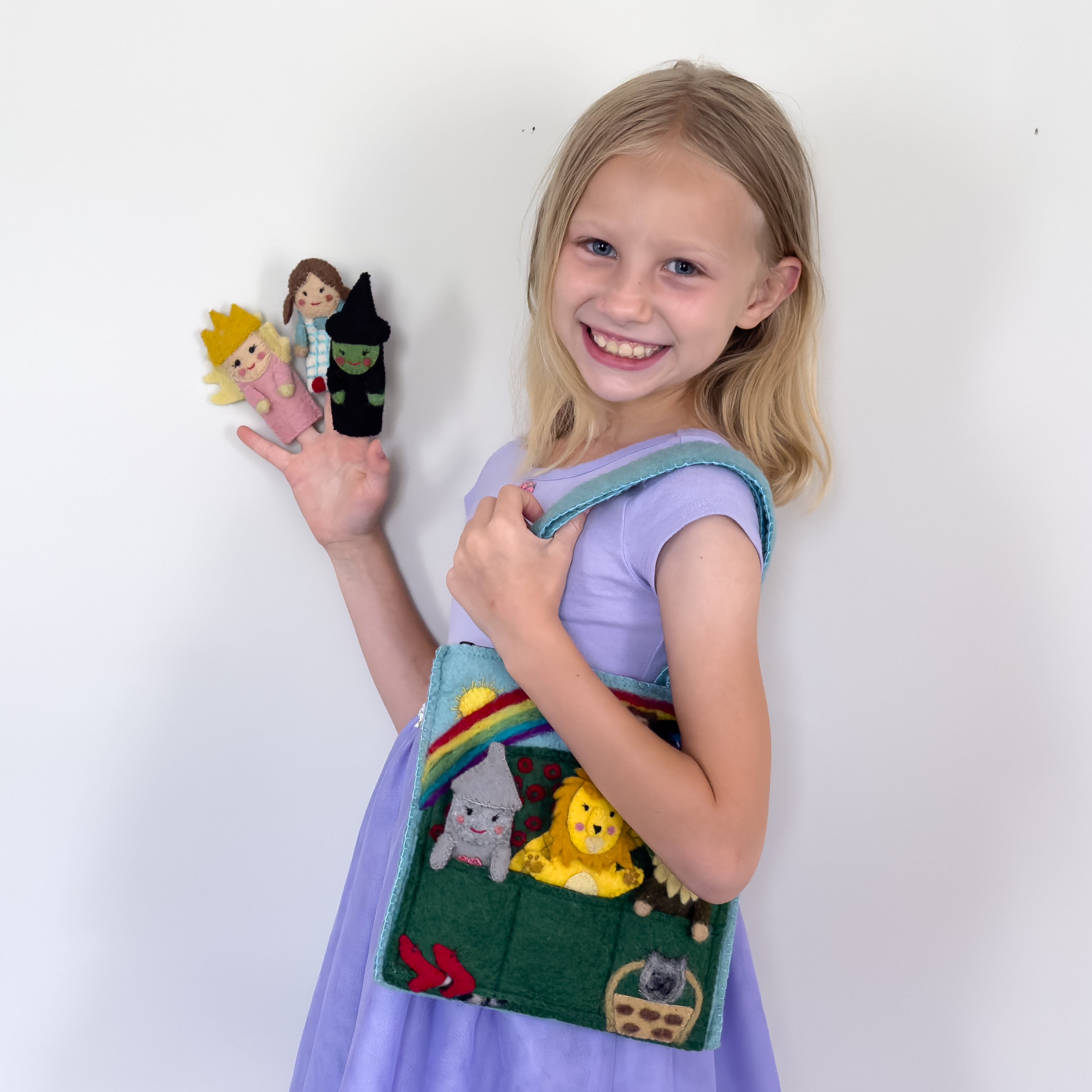 Young girl holding a colorful handmade fair trade felt bag with character designs, smiling against a white background | Global Goods Partners