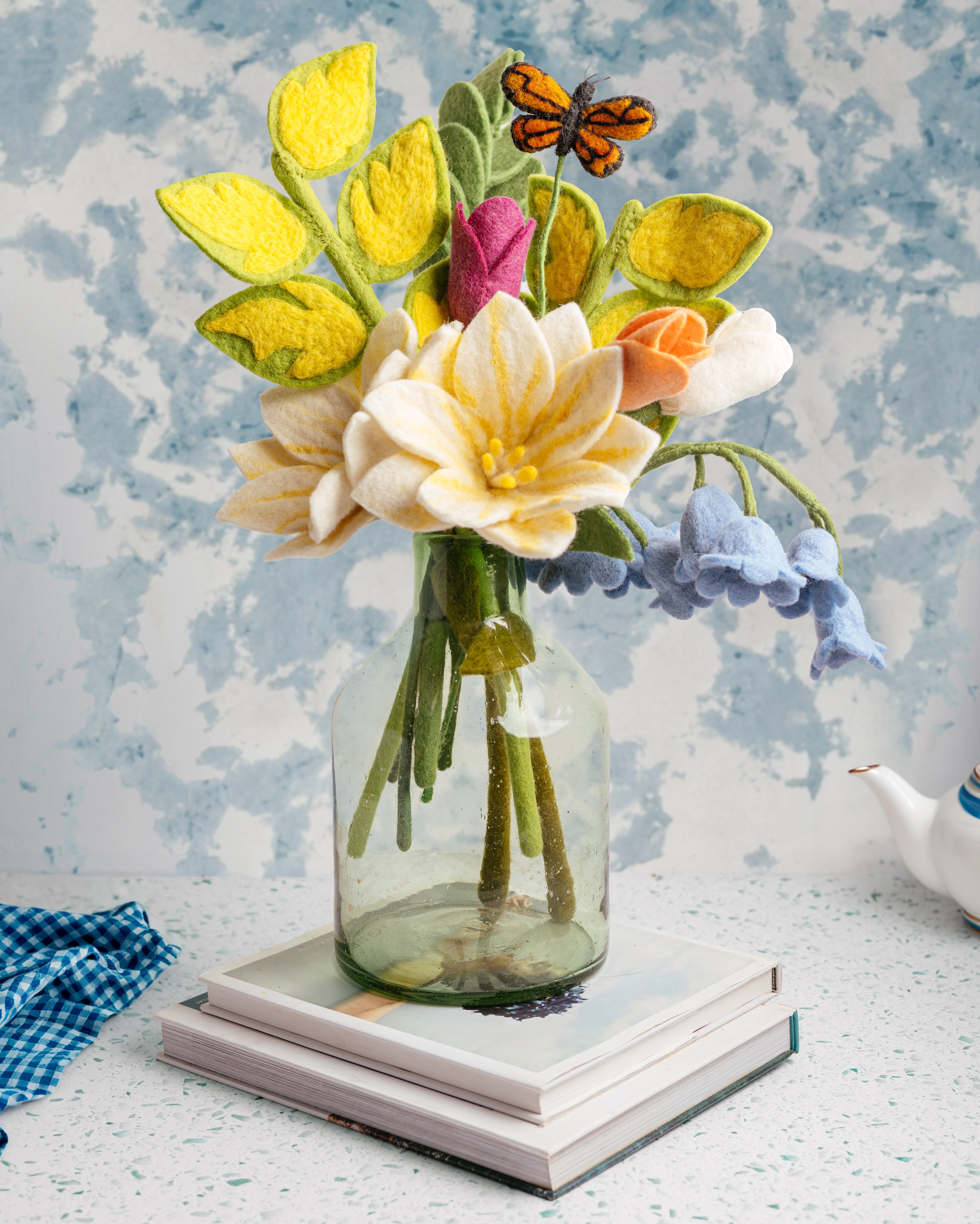 Felted flower arrangement in a glass vase on a textured surface with a felt butterfly all fair trade and handmade | Global Goods Partners