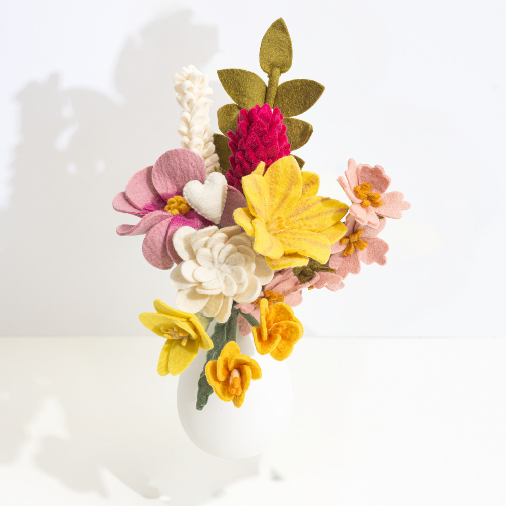 Colorful handmade felt flower arrangement in a white vase on a light background | Global Goods Partners