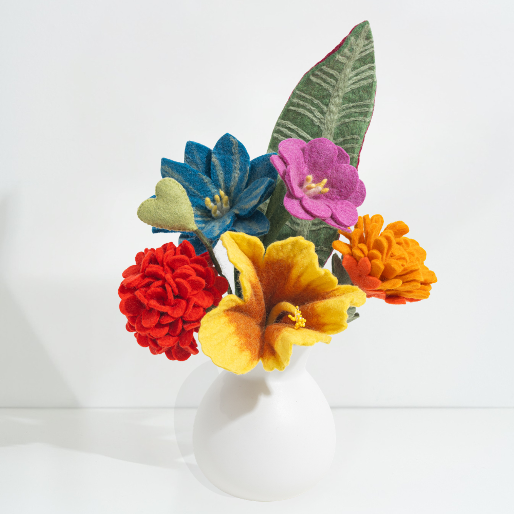 Vibrant, rainbow color felt flowers in a white vase on a light background, all handmade by women artisans | Global Goods Partners