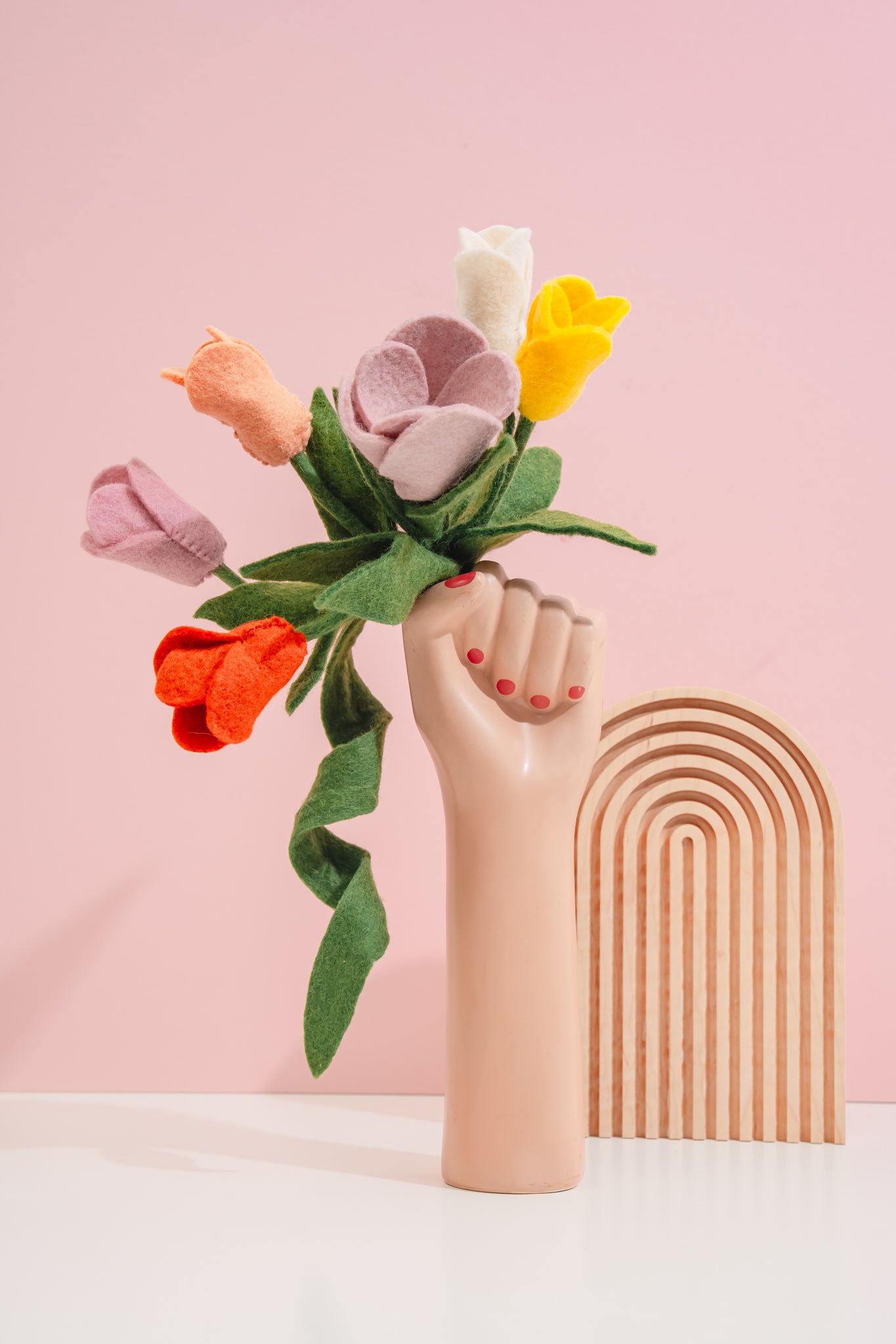 Handmade felt flower bouquet in a hand-shaped vase against a pink background | Global Goods Partners