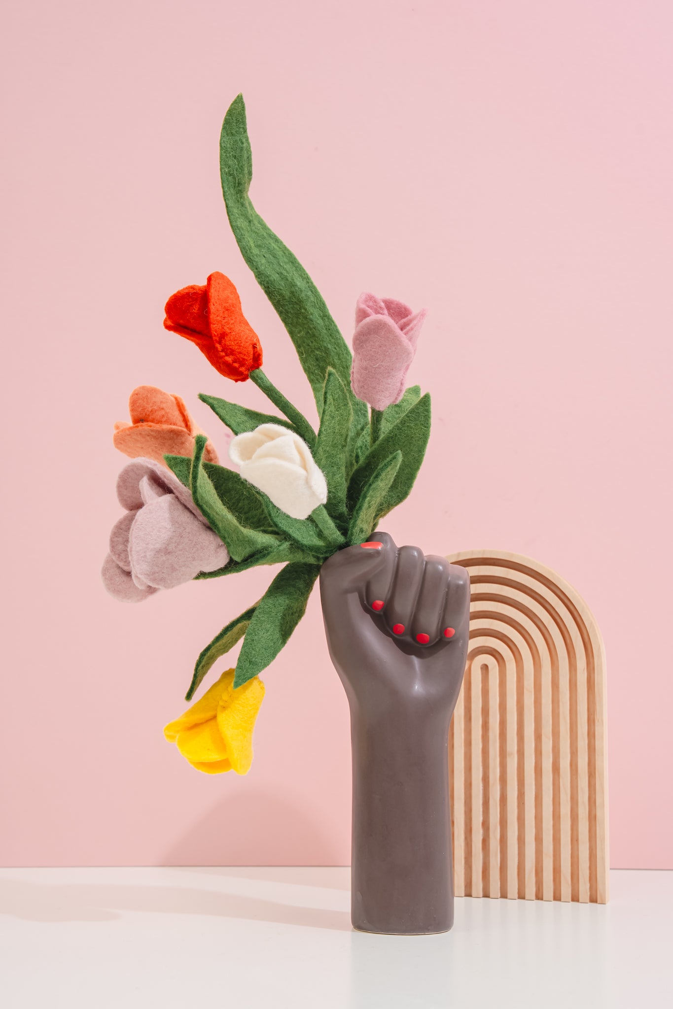 Black ceramic hand holding a bouquet of colorful felt flowers against a pink background, fair trade and made in Nepal | Global Goods Partners