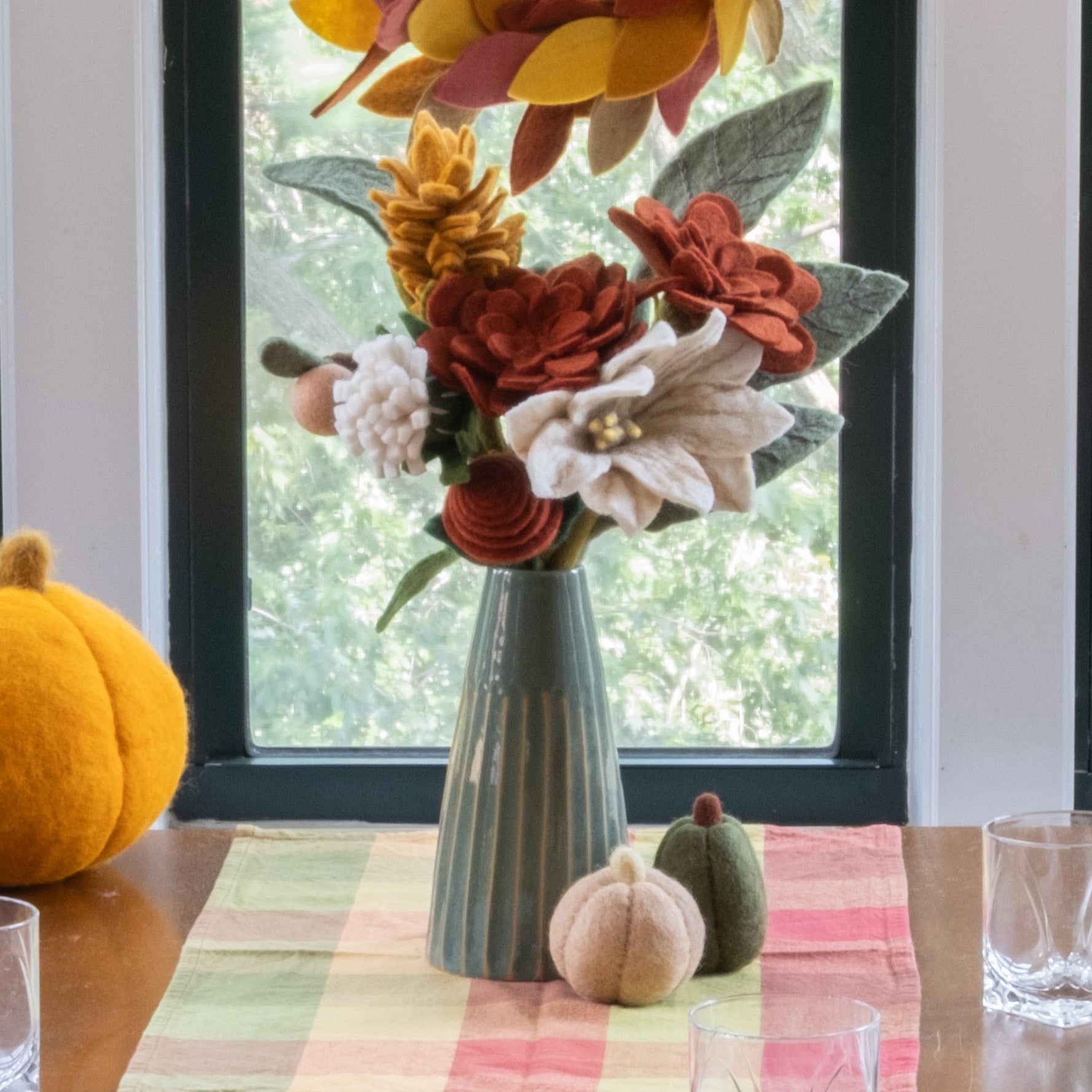 Dining room table set for a meal with autumn decorations, including pumpkins and floral arrangements, in front of a large window.