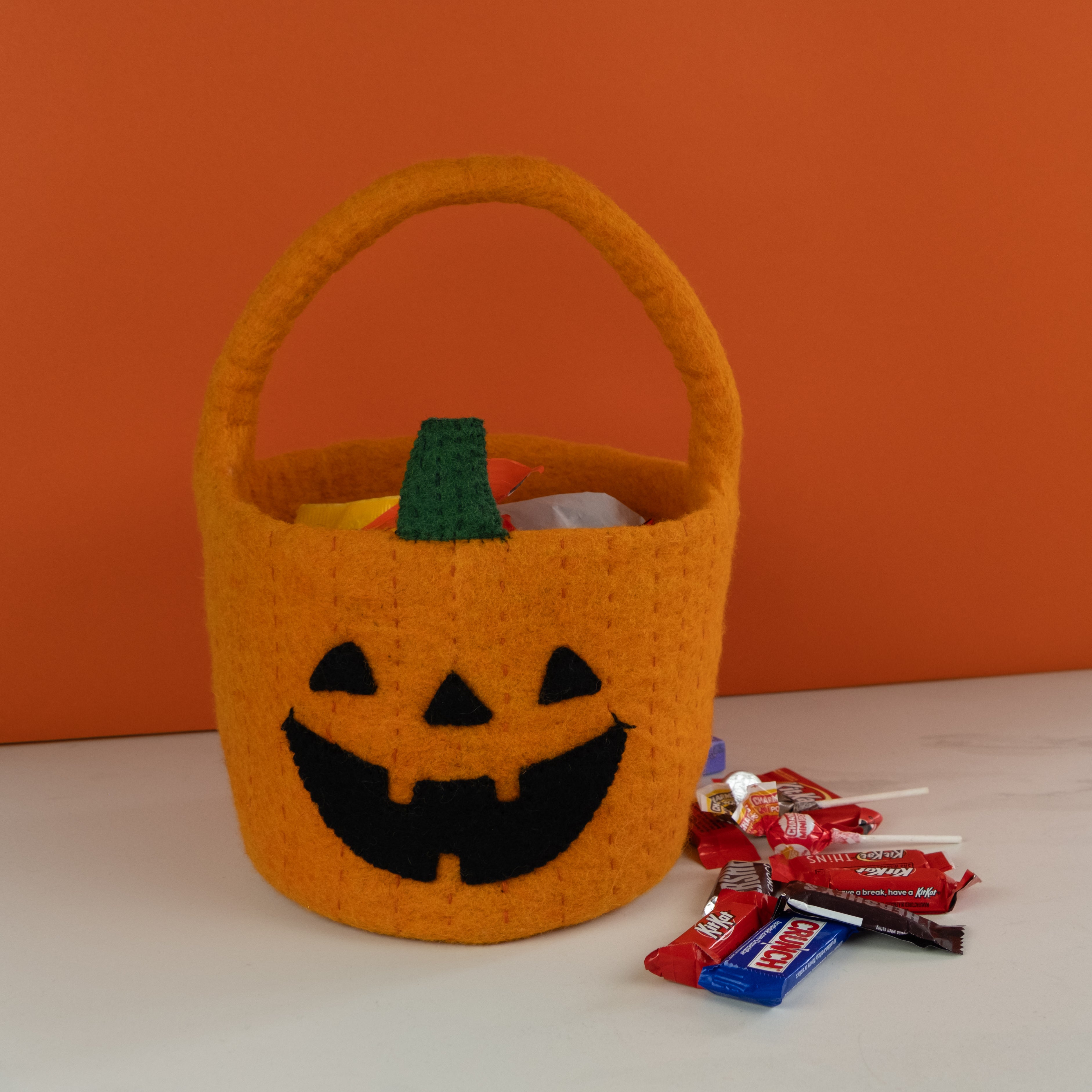 Orange Halloween candy basket with a jack-o'-lantern face on an orange background - Global Goods Partners