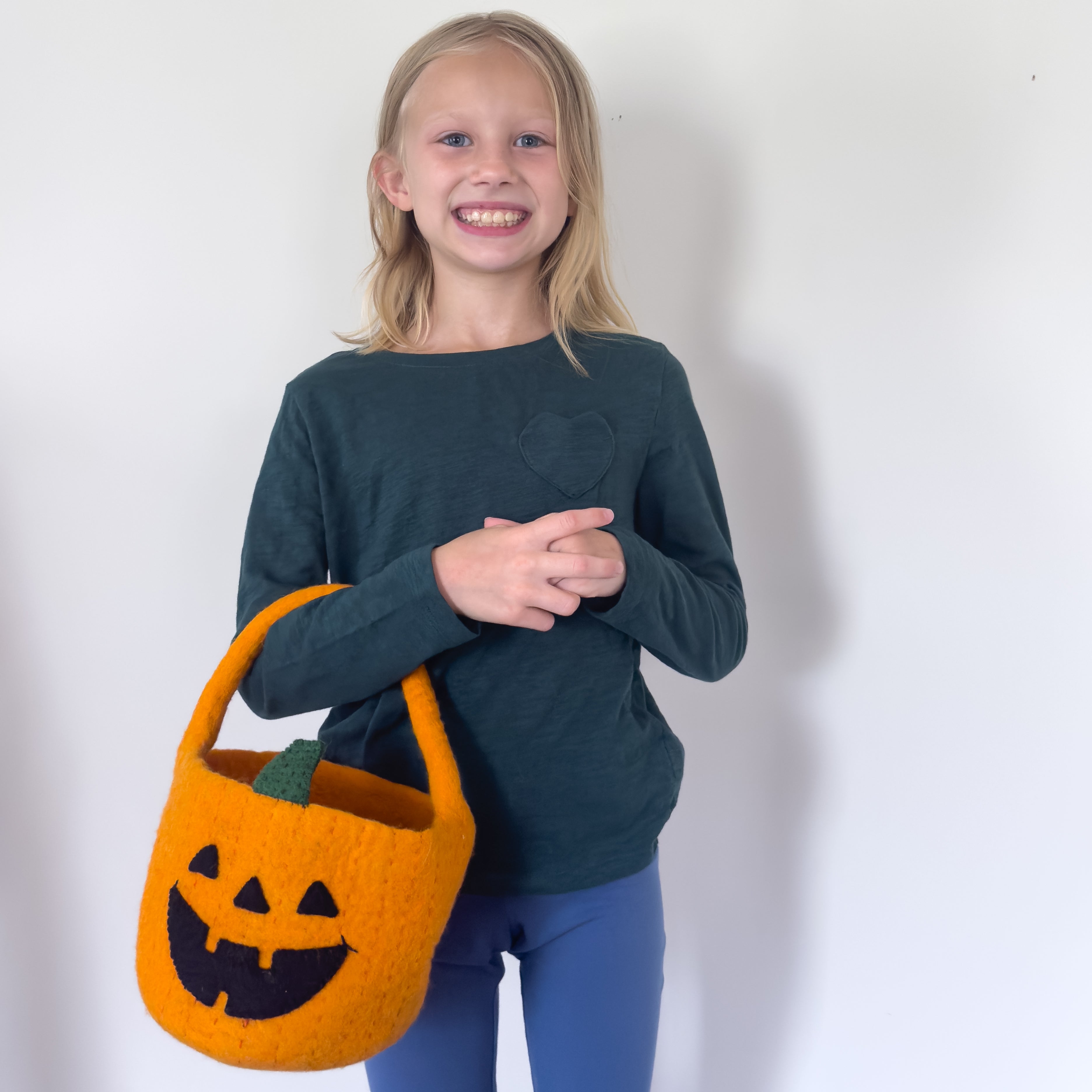 Young girl holding a fair trade felt orange Halloween candy bag against a white background - Global Goods Partners