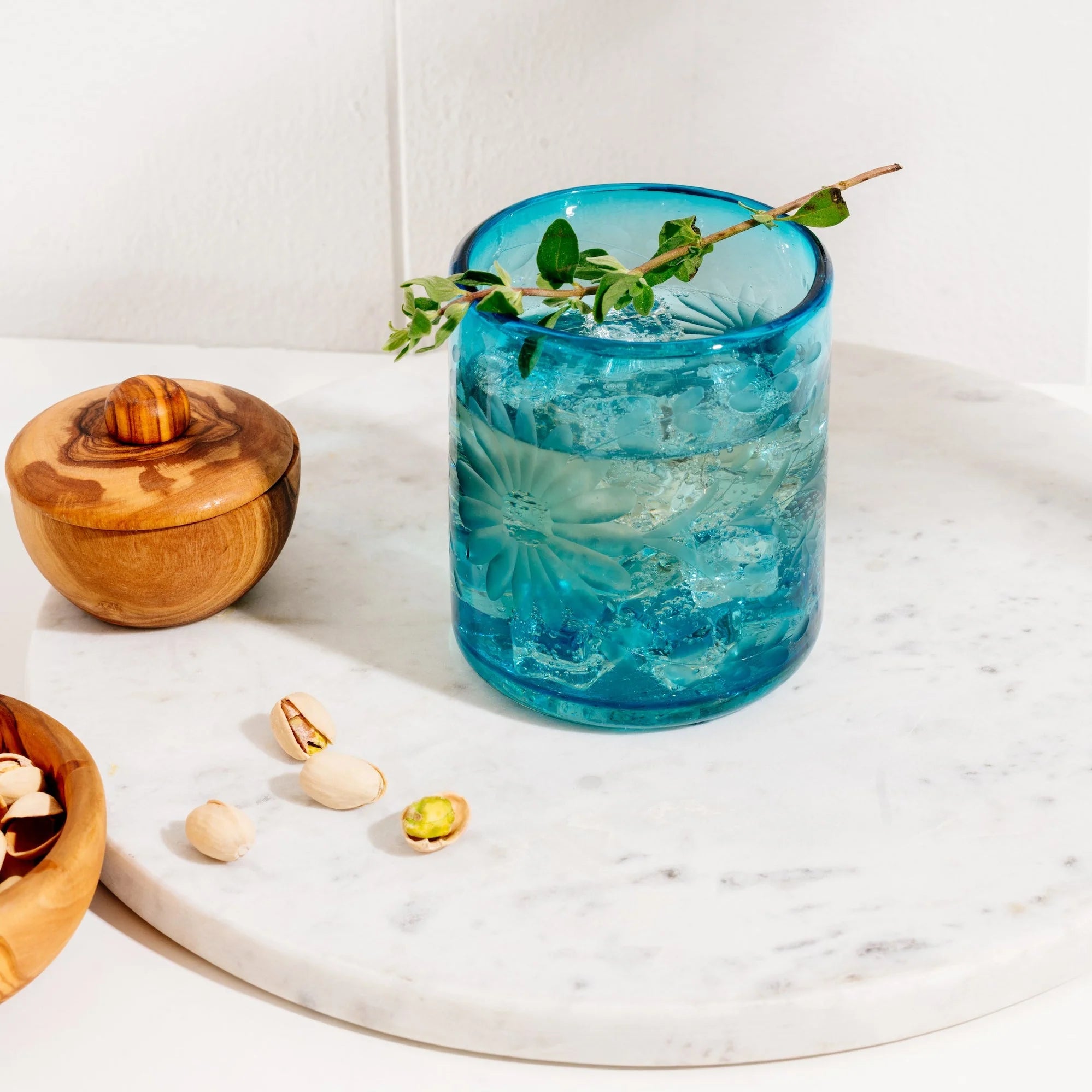 Blue glass with floral design on a marble surface with wooden bowl and nuts. Fair trade glassware | Global Goods Partners