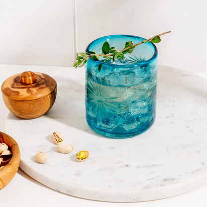 Blue glass with floral design on a marble surface with wooden bowl and nuts. Fair trade glassware | Global Goods Partners