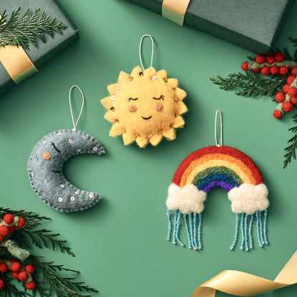 Handmade, fair trade felt ornaments shaped like a sun, moon, and rainbow on a green background with gift boxes and berries | Global Goods Partners