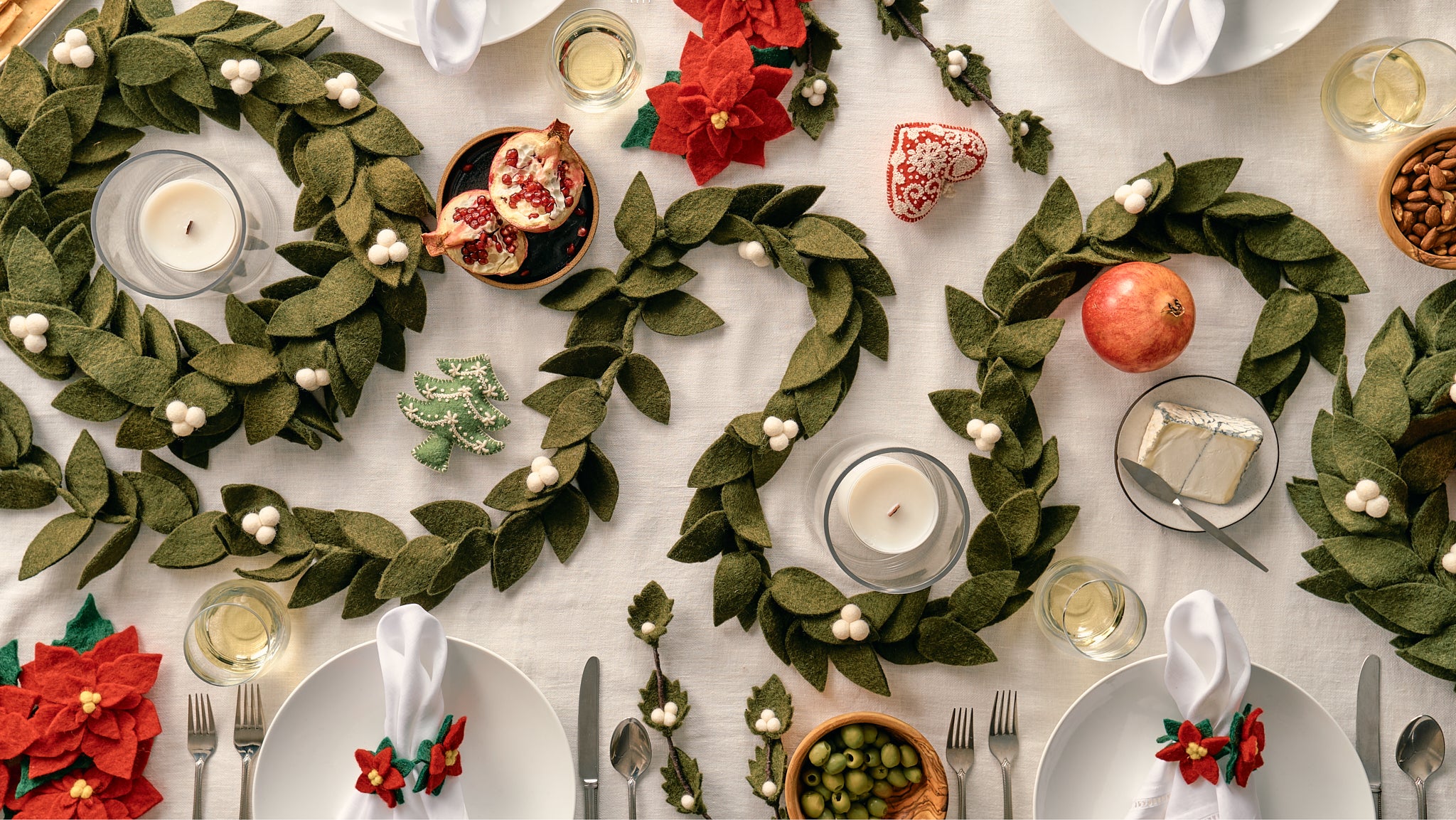 Decorative table setting with green wreaths, candles, and festive decorations on a white tablecloth. All products on table are handmade by women artisans in Nepal | Global Goods Partners