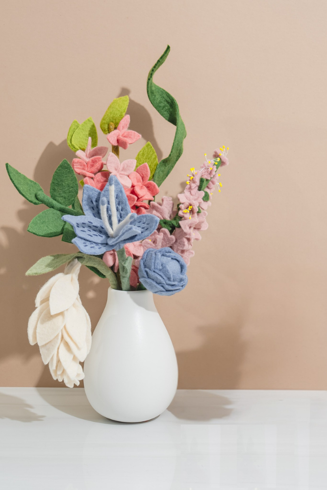 White vase with colorful felt flowers on a beige background, handmade by women artisans in Nepal | Global Goods Partners