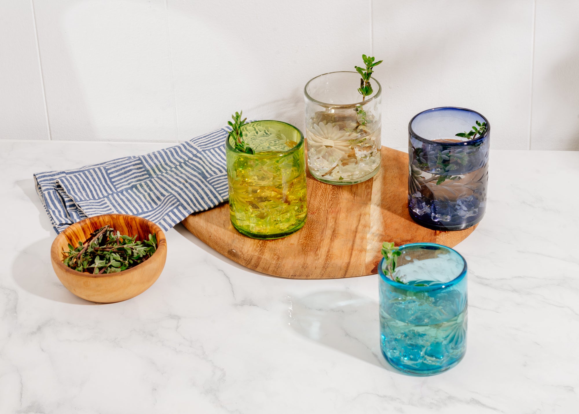 Four colorful glass tumblers with herbs on a marble surface, handmade in Mexico | Global Goods Partners
