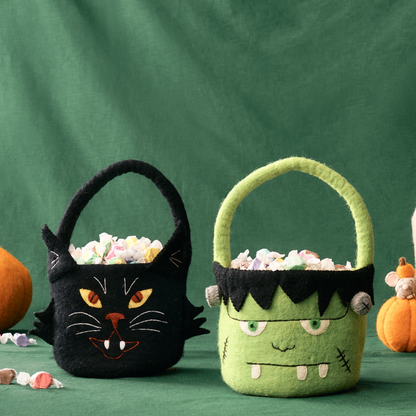 Black cat and green Frankenstein Halloween candy baskets on a green background with pumpkins. Handmade by women artisans in Nepal | Global Goods Partners