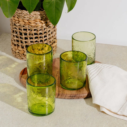 Green recycled glass tumblers on a wooden board with a woven basket and plant in the background | Global Goods Partners