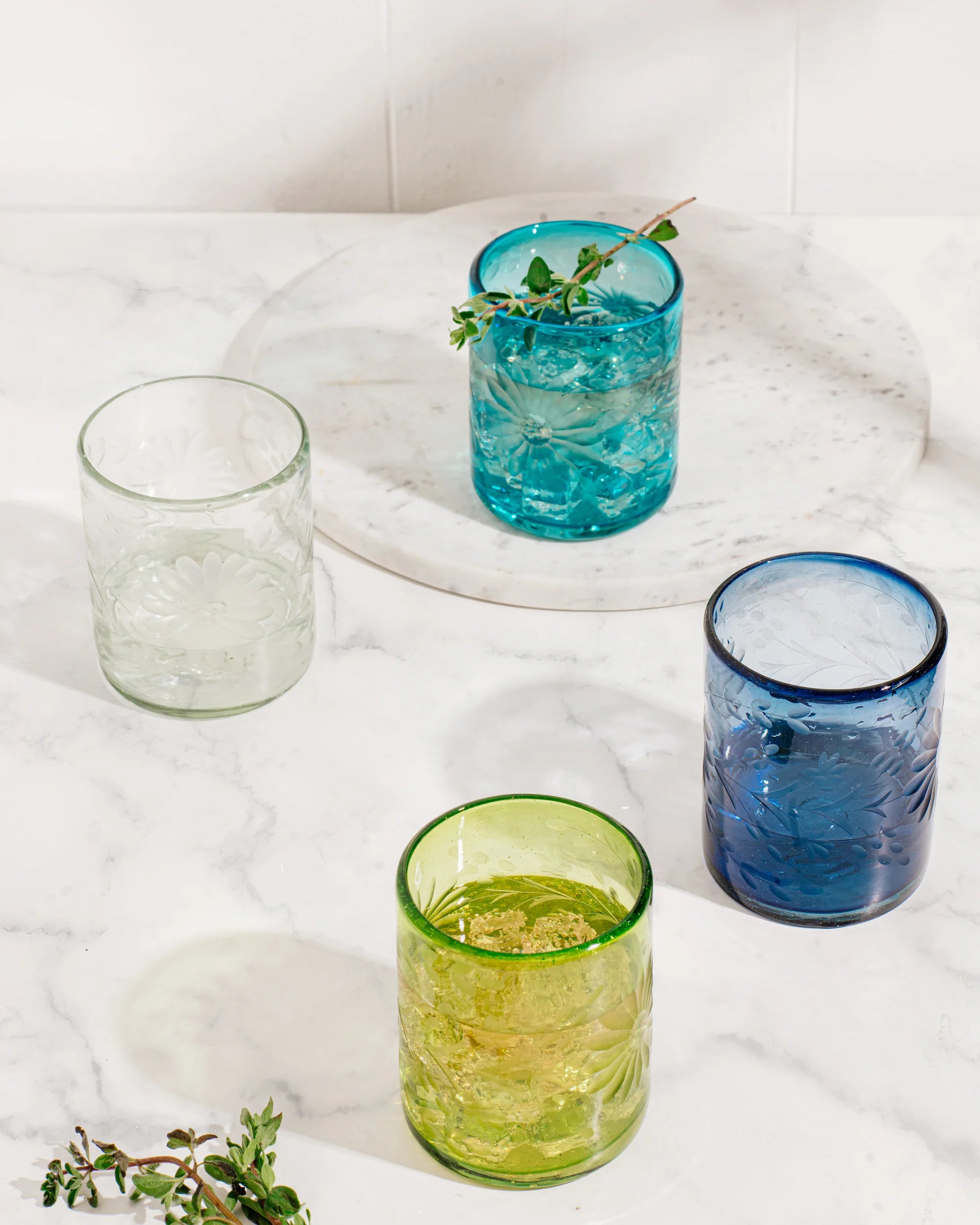 Four colorful glass tumblers on a white surface with greenery, all fair trade  | Global Goods Partners