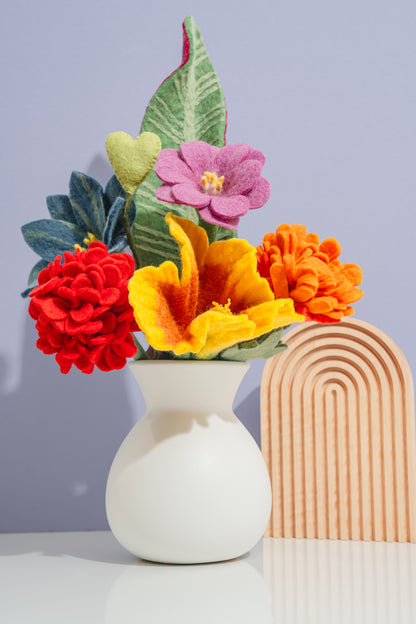 Colorful felt flower bouquet in a rainbow color palette in a white vase with a rainbow arch decoration on a light gray background | Global Goods Partners