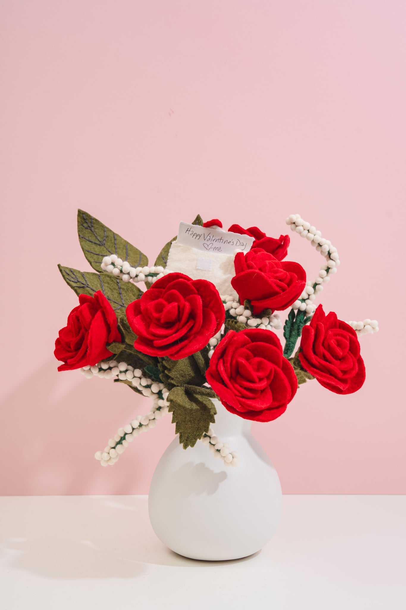 White vase with red handmade felt fair trade flowers on a pink background, product made by women artisans in Nepal | Global Goods Partners