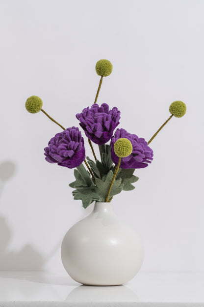 White vase with vibrant purple flowers and thin green stems on a white background. Felt flowers handmade in Nepal | Global Goods Partners