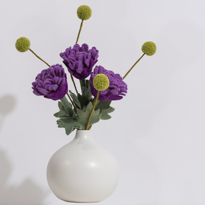 A highly structured and artistic arrangement of purple felt flowers and green felt stems on a light gray background in a white vase | Global Goods Partners