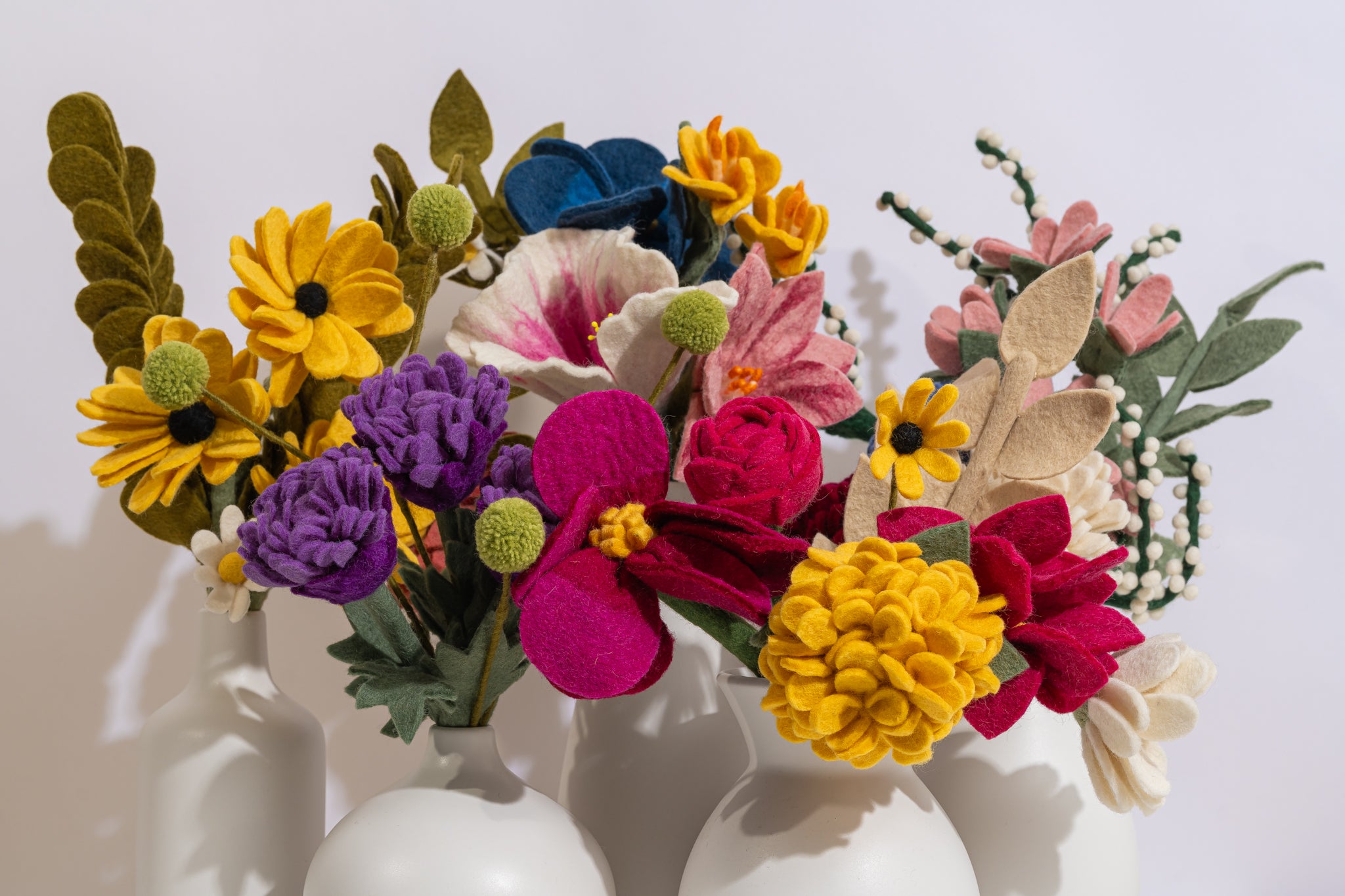 Colorful felt flower arrangements on white vases against a white background | Global Goods Partners