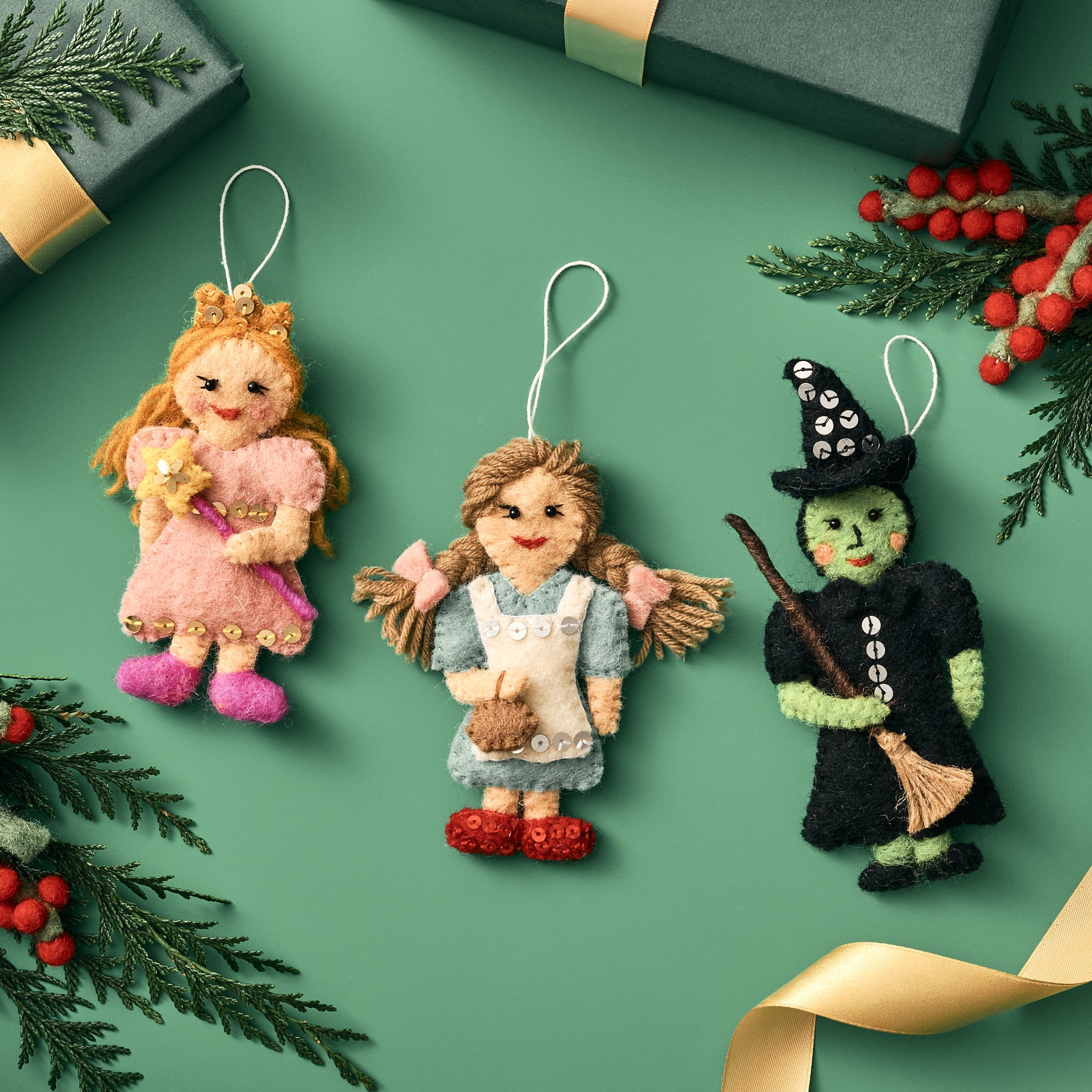 Three Wizard of Oz Christmas ornaments on a green background with decorative elements. Handmade by women artisans in Nepal | Global Goods Partners