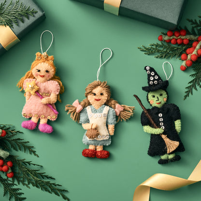 Three Wizard of Oz Christmas ornaments on a green background with decorative elements. Handmade by women artisans in Nepal | Global Goods Partners