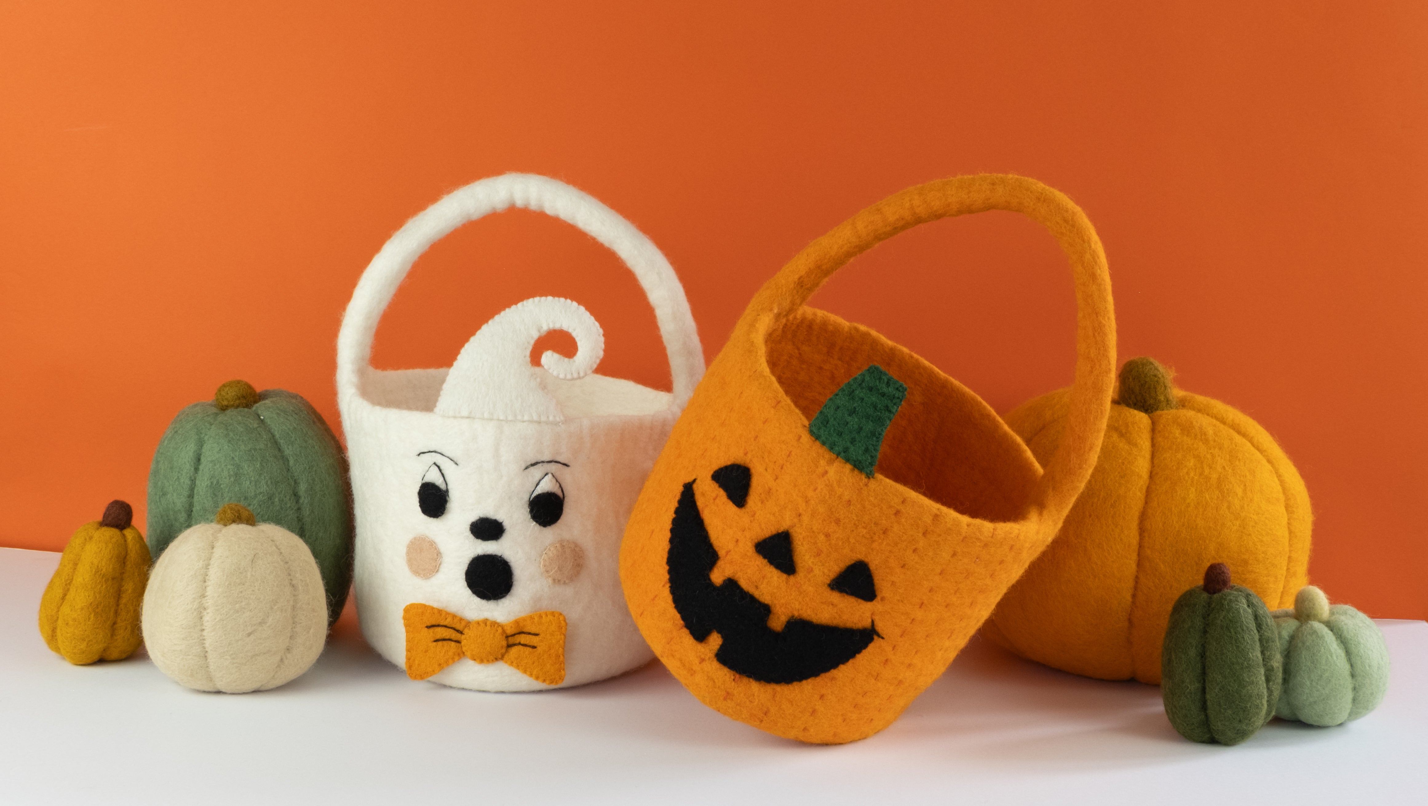 Felt Halloween baskets with pumpkin and ghost designs on an orange background. Handmade in Nepal - Global Goods Partners